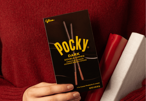 A person with a red sweater is holding a Pocky Dark Double Dipped box along with a red book and a white book.