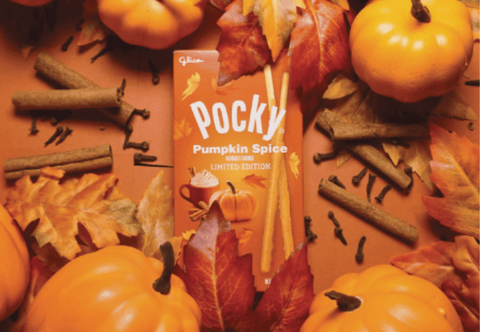 A box of Pocky Pumpkin Spice surrounded by fall leaves, pumpkins, and cinnamon sticks in orange background 