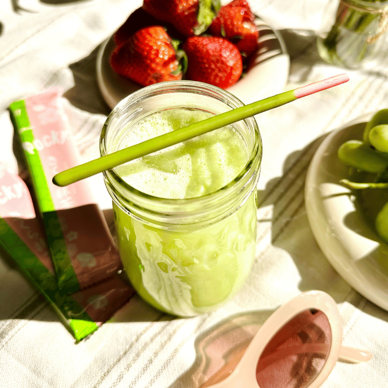 Matcha latte in a mason jar with a Pocky Cherry Blossom Matcha stick, surrounded by strawberries and grapes on a picnic blanket.