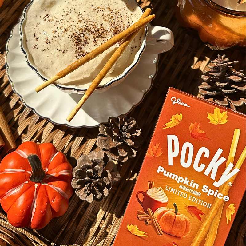 A lifestyle image featuring a box of Pocky Pumpkin Spice Limited Edition next to a cup of hot pumpkin spice latte with the two Pocky Pumpkin Spice sticks.