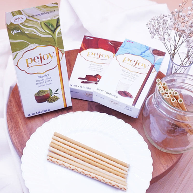 Pejoy Matcha, Chocolate, and Milk & Cookies on a wooden board with a vase of flowers in the background.