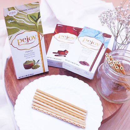 Pejoy Matcha, Chocolate, and Milk & Cookies on a wooden board with a vase of flowers in the background.