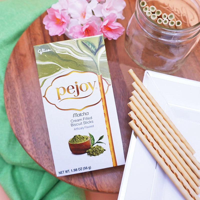 A box of Pejoy Matcha on a wooden board with a glass jar and plate of Pejoy Matcha sticks.