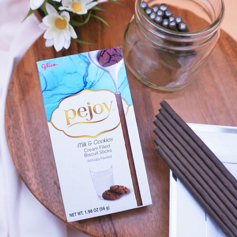 A box of Pejoy Milk & Cookies biscuit sticks on a wooden surface with a jar and plate of Pejoy Milk & Cookies.