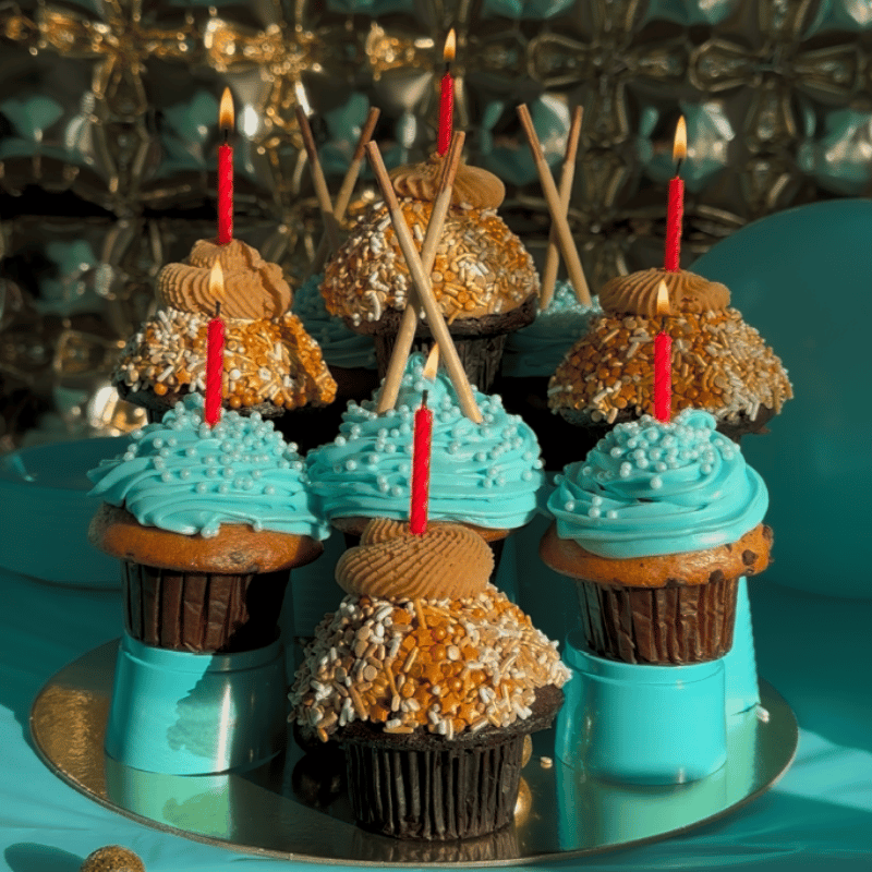 Decorative cupcakes with blue frosting and Pocky Peanut Butter sticks on a reflective surface.